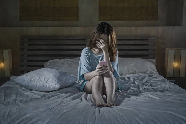 サイバーいじめや失恋の絶望的な女性表現でうつ病の苦しみの夜感悲しみと落ち込んで被害者でベッドで泣いている携帯電話を使用して若い落ち込んでアジア中国の女の子 — ストック写真