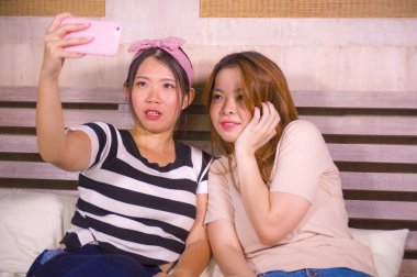 ev yatak yatak kadın dostluk ve sosyal medya bağımlılık kavramı üzerinde oturan cep telefonu kamera ile selfie portre fotoğraf çekme oturan iki genç mutlu ve pretty Asya Koreli kız arkadaşım