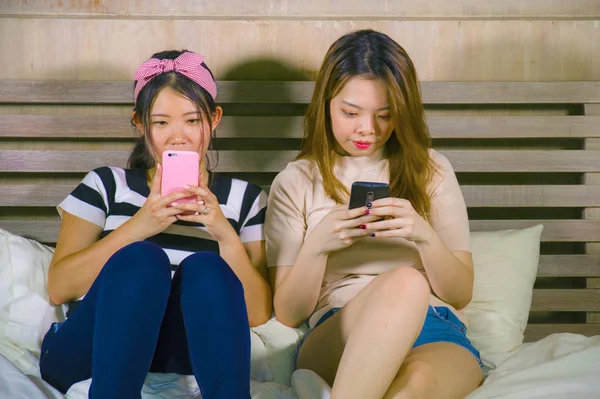 つ若い幸せとはかなりアジア韓国のガール フレンドに座って笑って 話を持っている家の寝室で楽しい女性友情でベッドの上に座って携帯電話でインターネットのソーシャル メディア アプリを使用して — ストック写真