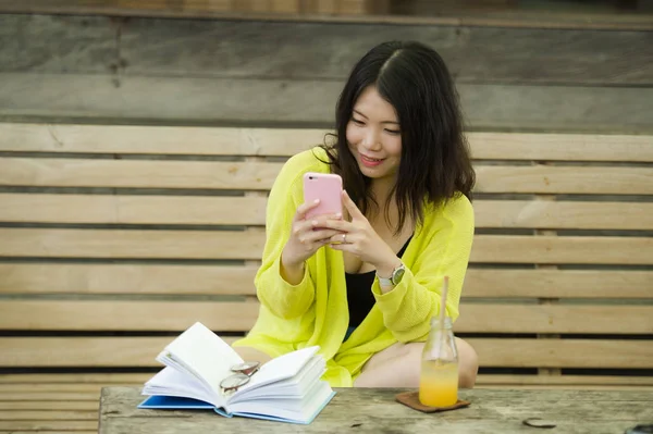 年轻美丽快乐的亚洲华裔妇女坐在复古木材咖啡店放松和快乐 喝橙汁阅读新书 并在女孩休闲周末生活方式中使用手机 — 图库照片