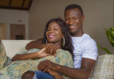 mutlu ve başarılı romantik Afro-Amerikan çift aşk rahat oturma birlikte oturma odası kanepe rahat kanepede sarılma ve neşeli gülümseyen genç yaşam tarzı ev portresi