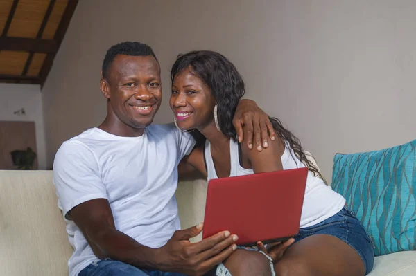 lifestyle home portrait of young happy and beautiful black afro American couple in love enjoying at living room sofa couch with laptop computer laughing and having fun networking