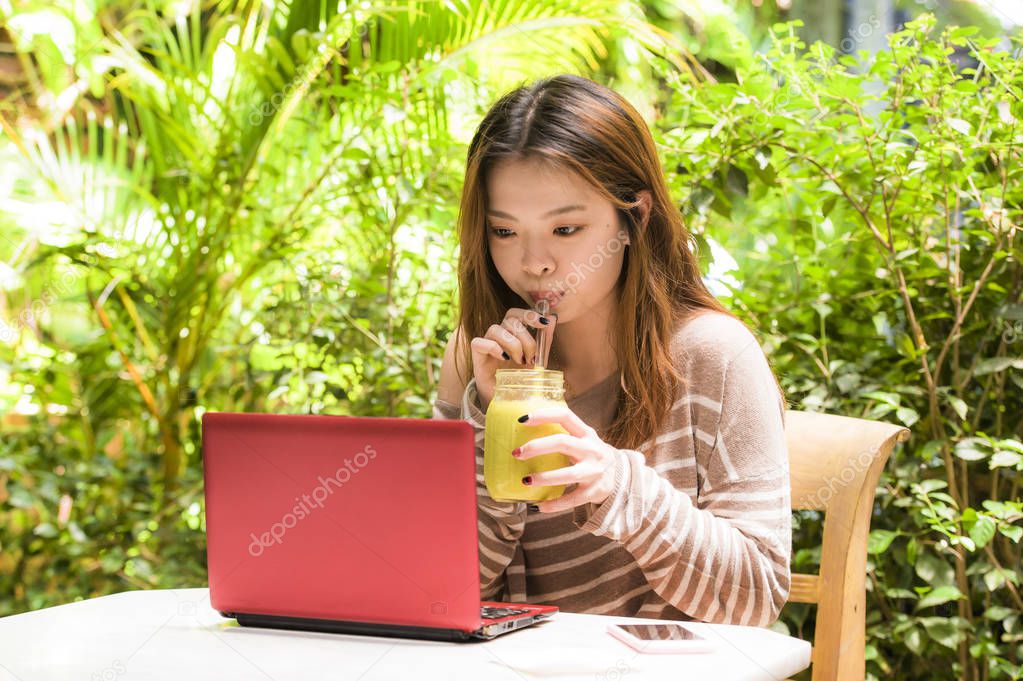 lifestyle portrait of young beautiful and happy Asian Chinese student girl working outdoors at sweet coffee shop garden with laptop computer or studying relaxed and concentrated