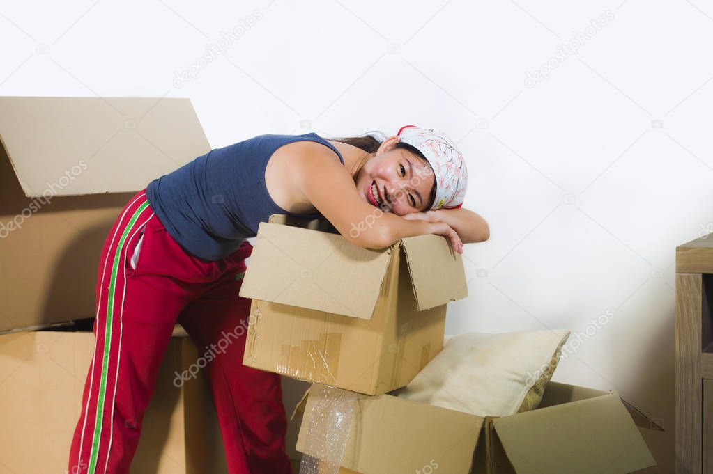 young beautiful and happy Asian Korean woman excited at home living room floor unpacking belongings from cardboard boxes moving to new apartment in first house and property investment concept