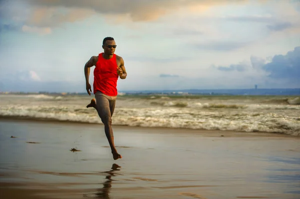 young attractive fit athletic and strong black afro American man running at the beach training hard and sprinting on sea water in professional athlete lifestyle and ripped runner workout