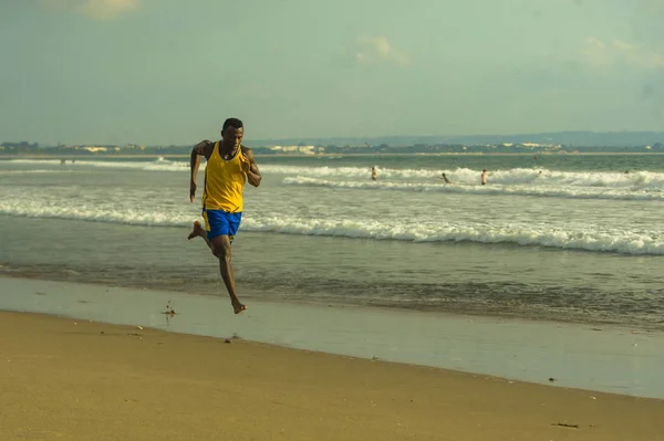 young attractive fit athletic and strong black African American man running at the beach training hard and sprinting on sea water in professional athlete lifestyle and ripped runner workout