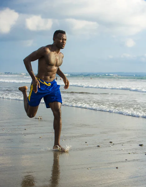 young attractive fit athletic and strong black African American man running at the beach training hard and sprinting on sea water in professional athlete lifestyle and ripped runner workout