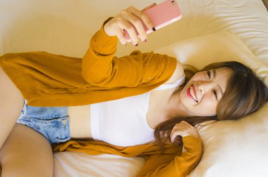 telefon kullanarak genç çekici ve rahat Asyalı Koreli kız telefon evde yatak keyfi internet online dating uygulaması veya genç öğrenci yaşam tarzı kavramı yatakta yatan sosyal medya