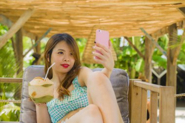 yaşam tarzı tatil seyahat keyfi hareket eden telefon fotoğraf makinesi ile selfie fotoğrafta tropikal resort Bahçe içme Hindistan cevizi suyu genç mutlu ve çekici Çinli öğrenci kız portresi