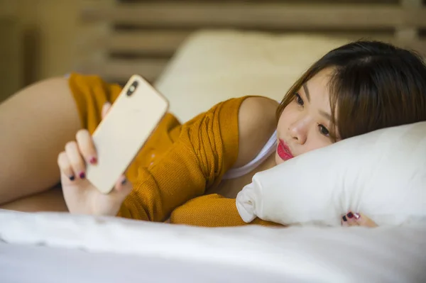 魅力的でリラックスしたアジア中国少女使用して 携帯電話自宅寝室楽しんでインターネット オンライン出会い系アプリやソーシャル メディアの 代学生ライフ スタイル コンセプトでベッドの上に横になっています — ストック写真