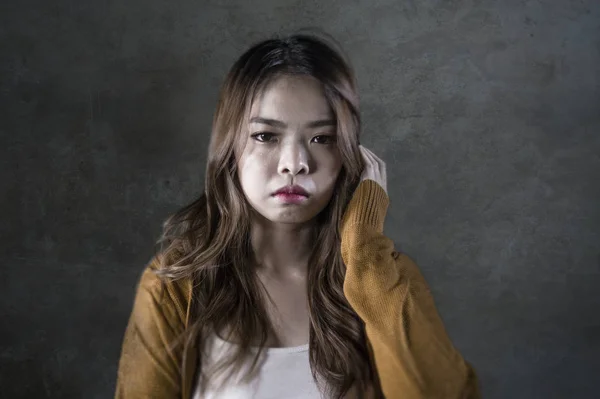 young crazy desperate and sad Asian Korean woman looking depressed and helpless feeling anguish and pain on isolated dark background in pain face expression suffering depression