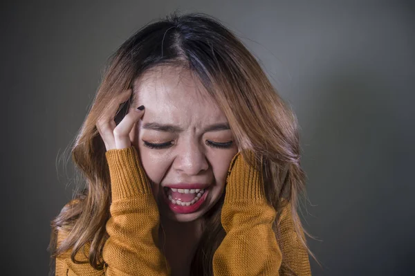 young crazy desperate and upset Asian Korean woman screaming scared and anxious feeling anger and pain isolated on dark background on dramatic pain face expression in depression concept