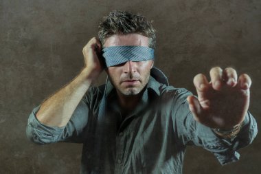 young lost and confused man blindfolded with necktie playing internet trend dangerous viral challenge with eyes blind acting doubtful guided by intuition isolated on dark background clipart