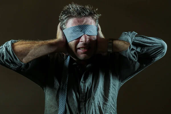 young lost and confused man blindfolded with necktie playing internet trend dangerous viral challenge with eyes blind acting doubtful guided by intuition isolated on dark background