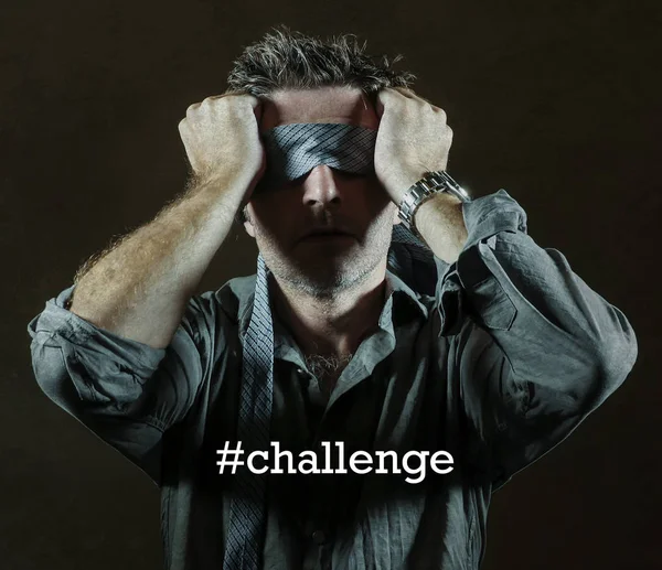 young lost and confused man blindfolded with necktie playing internet trend dangerous viral challenge with eyes blind acting doubtful guided by intuition isolated on dark background