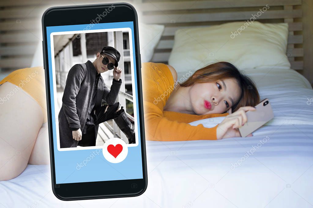 young beautiful and happy Korean woman in bed using mobile phone doing video call or flirting online via social media dating app with cool man in Asian couple internet love relationship concept