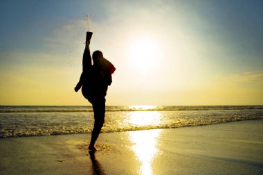 Savunma kavramı içinde güzel bir plaj batımında Islam türban başörtüsü eğitim dövüş sanatları karate tekme saldırı ve fitness egzersiz genç zinde ve agresif Müslüman kadın silüeti kaplı