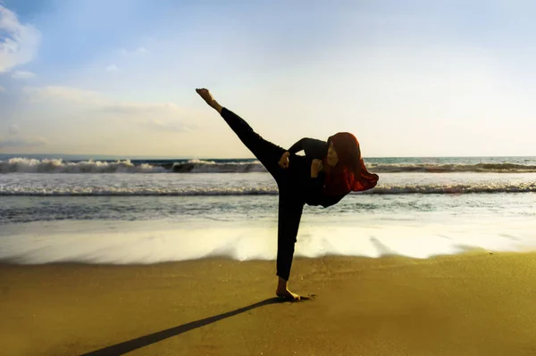 silhouette of young fit and aggressive Muslim woman covered in Islam hijab head scarf training martial arts karate kick attack and fitness workout at beautiful beach sunset in defense concept