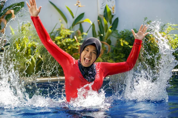 su geleneksel İslam'ın başörtüsü ve tatil gezi zevk İslam mayo giyen resort yüzme havuzu sıçramasına ve sahip eğlenceli heyecan ile oynayan genç mutlu ve neşeli Müslüman kadın