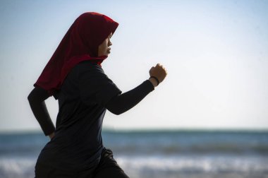 çalışan ve geleneksel Arap spor kıyafetlerle fitness egzersiz ve kilo kaybı kavramında sahilde koşu Islam türban Başörtüsü Müslüman kadında genç sağlıklı ve aktif atlet