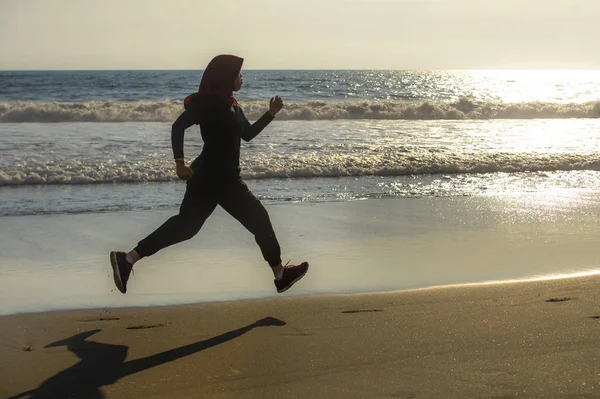 young healthy and active runner Muslim woman in Islam hijab head scarf running and jogging on the beach wearing traditional arab sport clothes in fitness workout and weight loss concept