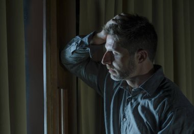 dramatic portrait of young handsome sad and depressed man desperate suffering depression problem feeling broken heart pain looking desperate at home by curtains window at night