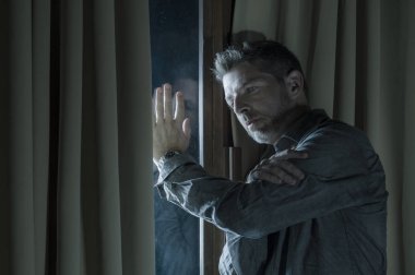 dramatic portrait of young handsome sad and depressed man desperate suffering depression problem feeling broken heart pain looking desperate at home by curtains window at night