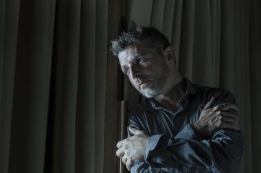 dramatic portrait of young handsome sad and depressed man desperate suffering depression problem feeling broken heart pain looking desperate at home by curtains window at night