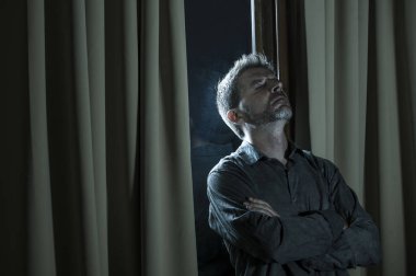 dramatic portrait of young handsome sad and depressed man desperate suffering depression problem feeling broken heart pain looking desperate at home by curtains window at night