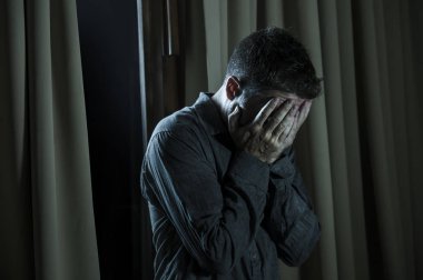 dramatic portrait of young handsome sad and depressed man desperate suffering depression problem feeling broken heart pain looking desperate at home by curtains window at night