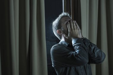 dramatic portrait of young handsome sad and depressed man desperate suffering depression problem feeling broken heart pain looking desperate at home by curtains window at night