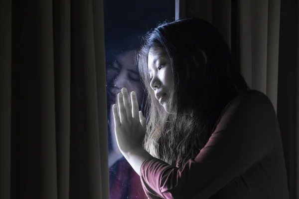 dramatic indoors portrait of young sad and depressed Asian Japanese woman crying desperate broken heart suffering depression and anxiety in dark light at home curtains window in sadness concept