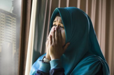 İslam'ın geleneksel türban başörtüsü ev pencere duygu acı depresyon kriz ve anksiyete sorunu ağlıyor yardıma muhtaç hasta adlı genç üzgün ve depresyonda Müslüman kadın portresi yaşam tarzı