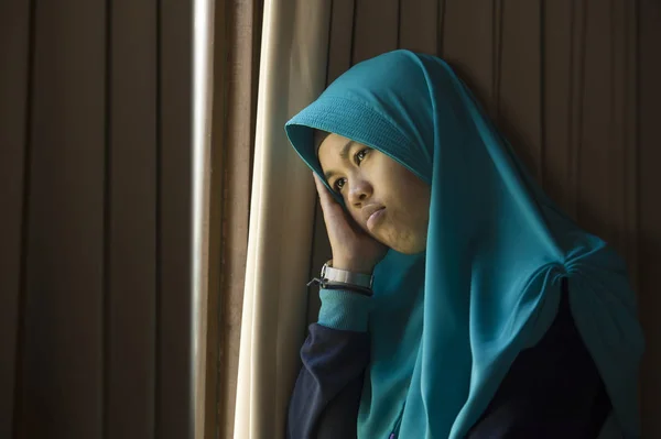 年轻悲伤和沮丧的穆斯林妇女的生活方式肖像在伊斯兰教传统的 Hijab 头围巾在家里的窗口感到不适忍受抑郁症危机和焦虑问题周到和无助 — 图库照片