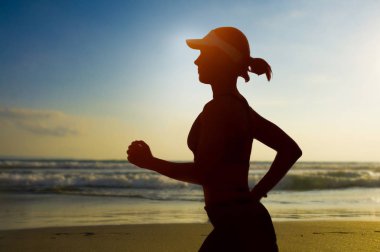 Genç zinde ve günbatımı Plaj Spor egzersiz ve sağlıklı yaşam konsepti içinde güzel bir gökyüzü altında çalışan fitness egzersiz yapıyor günü Amerikan kap eğitim çekici kadın silüeti
