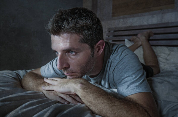 молодой грустный и депрессивный бессонный мужчина лежал на кровати беспокойный и вдумчивый дома спальня страдает депрессией проблема чувствует себя нездоровым и отчаянно разбитое сердце после развода отношений
