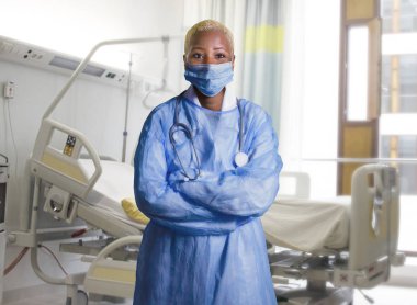 yüz maskesi ve hastane odasında izole sağlık iş kavramı kurumsal duran mavi önlük giyen genç çekici ve kendinden emin siyah Afro-Amerikan tıp Doktor