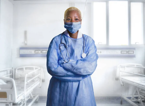 young attractive and confident black African American medicine doctor wearing face mask and blue scrubs standing corporate in health care work concept isolated at hospital room