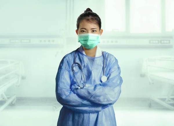 young confident and successful Asian Korean medicine doctor woman in hospital scrubs and mask posing isolated at clinic patient bed in medical health care as corporate physician portrait