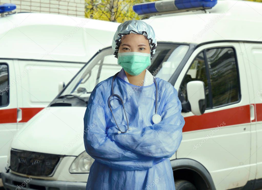 young confident and successful Asian Korean medicine doctor woman in hospital scrubs and mask posing outdoors with ER ambulance background in medical health care as emergency physician