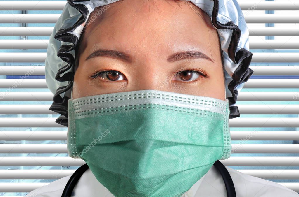 close up isolated portrait of young attractive and confident Asian Chinese medicine doctor woman in protective head cap face mask and scrubs with stethoscope as hospital health care staff