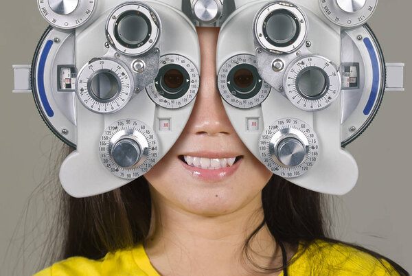young woman smiling happy looking through optometric hospital device and checking eyes having sight exam in ophthalmology health care isolated on grey background
