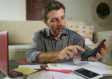 Genç yakışıklı ve mutlu başarılı adam hesap makinesi ve iç muhasebe evrakları yurtiçi ödemeleri vergi ve oturma odası evde oturan aylık iş gelir yapmak laptop ile