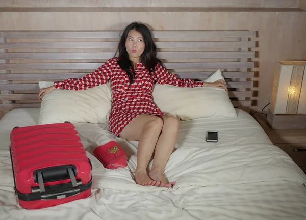 young beautiful and happy Asian Korean woman in chic dress sitting happy in room bed  with luggage after hotel check in excited and cheerful enjoying holidays travel in luxury destination concept