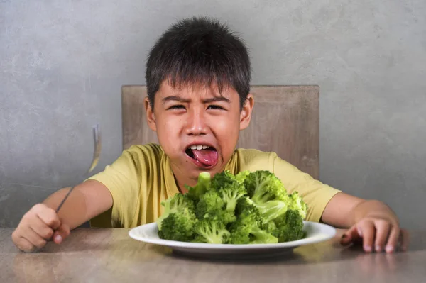 または 年古い動揺し うんざりするヒスパニック系の子供が不幸な子で生鮮食品を拒否する探しているブロッコリー プレートの前にテーブルの上に座って嫌い野菜コンセプトと健康的な栄養 — ストック写真