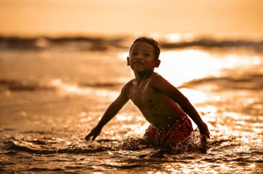 Silhouette genç çocuk mutlu ve sahilde su oynarken sıçramasına ücretsiz atlama ve having fun yaz tatilleri dalgalar deniz ile seyahat deli oynarken ve özgürlük hissi kavramı