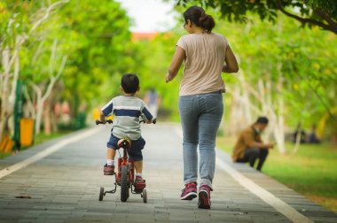 Görünüm yaşam tarzı portresi anne ve şehir parkında eğlenceli birlikte öğrenme bisiklet sürme ve annelik kavramı içinde çocuk sonra çalışan kadın çocuk sahibi genç mutlu oğul geri