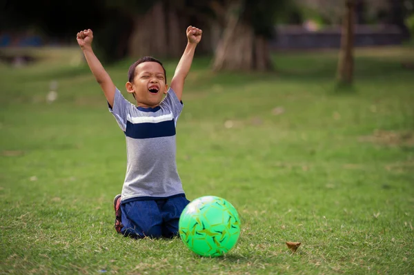 yaşam tarzı çimen Şehir Parkı 5 yaşında Asyalı çocuk mutlu ve heyecanlı futbol oynarken, resme skor gol çocuk spor pratik eğitim ve genç futbol fan kavramı kutlama silah yükseltme