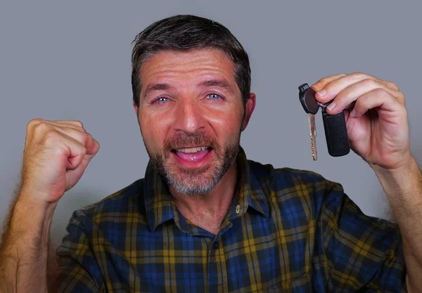 young happy and excited 30s or 40s attractive man holding car key celebrating buying new automobile or motorbike isolated on grey background