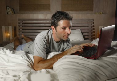 genç çekici ve rahat adam evde ağ yatak gece geç saatlerde dizüstü bilgisayar ya da çalışma zevk internet sosyal medya seyir üzerinde neşeli ve memnun mutlu yazarak üzerinde rahat yalan